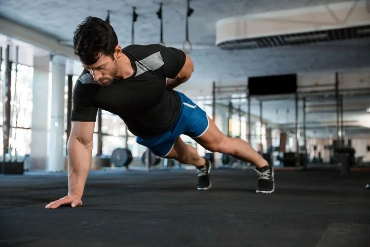 Athlet wearing blue shorts and black t-shirt doing one hand push-ups