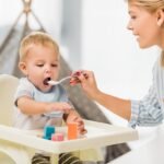 mother feeding son in highchair with baby food