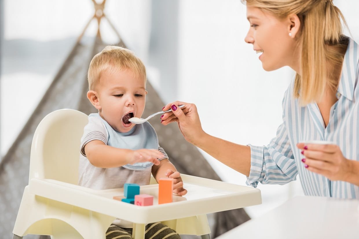 mother feeding son in highchair with baby food